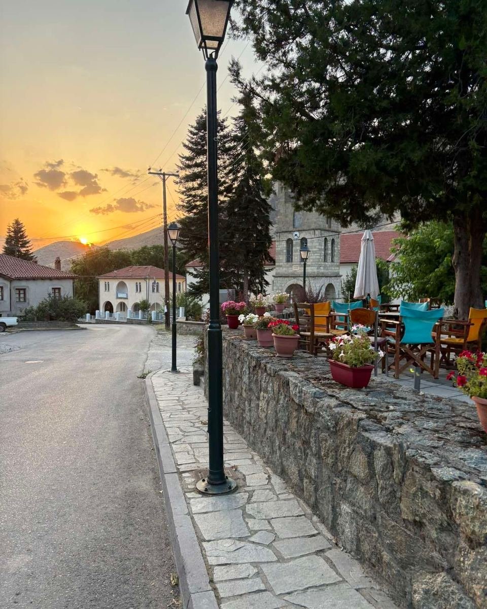 Ηλιοβασίλεμα σε δρόμο του χωριού, με φανοστάτη και πέτρινο τοίχο.